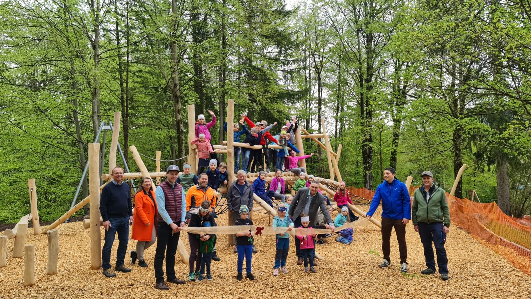Grainau, Kinderspielplatz, Klettergerüst mit vielen verschiedenen Modulen, Kinder die auf dem Gerüst stehen und sitzen, Erwachsene die bei der Einweihung das Band, welches ein Kind durchschneidet, halten