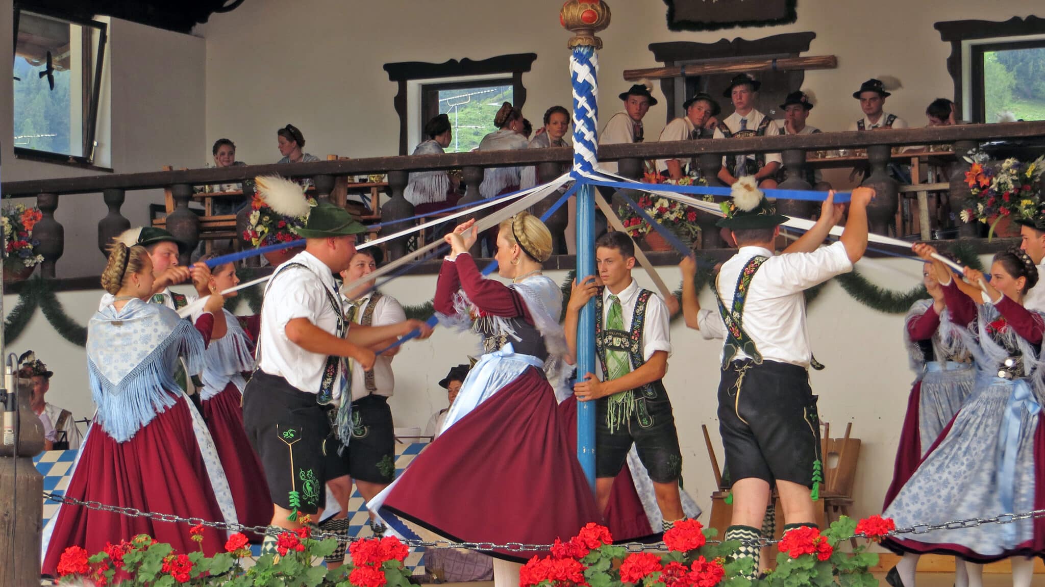 Grainau Parkfest. Grainauer Plattler bei einem traditionellen Tanz. Paare in Grainauer Tracht tanzen mit weißen und blauen Bändern die an einer Stange befestigt sind.