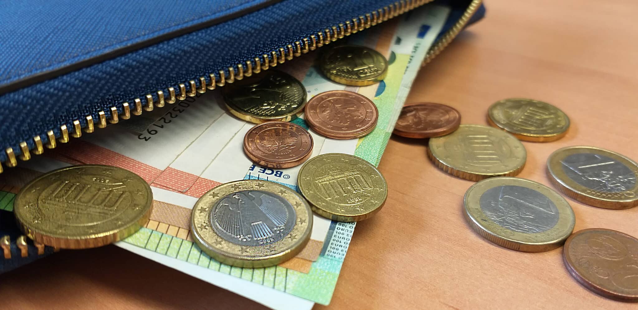 Grainau, Blaue Geldtasche geöffnet, Geldscheine und Münzen sind zu sehen, die aus der Geldtasche fallen