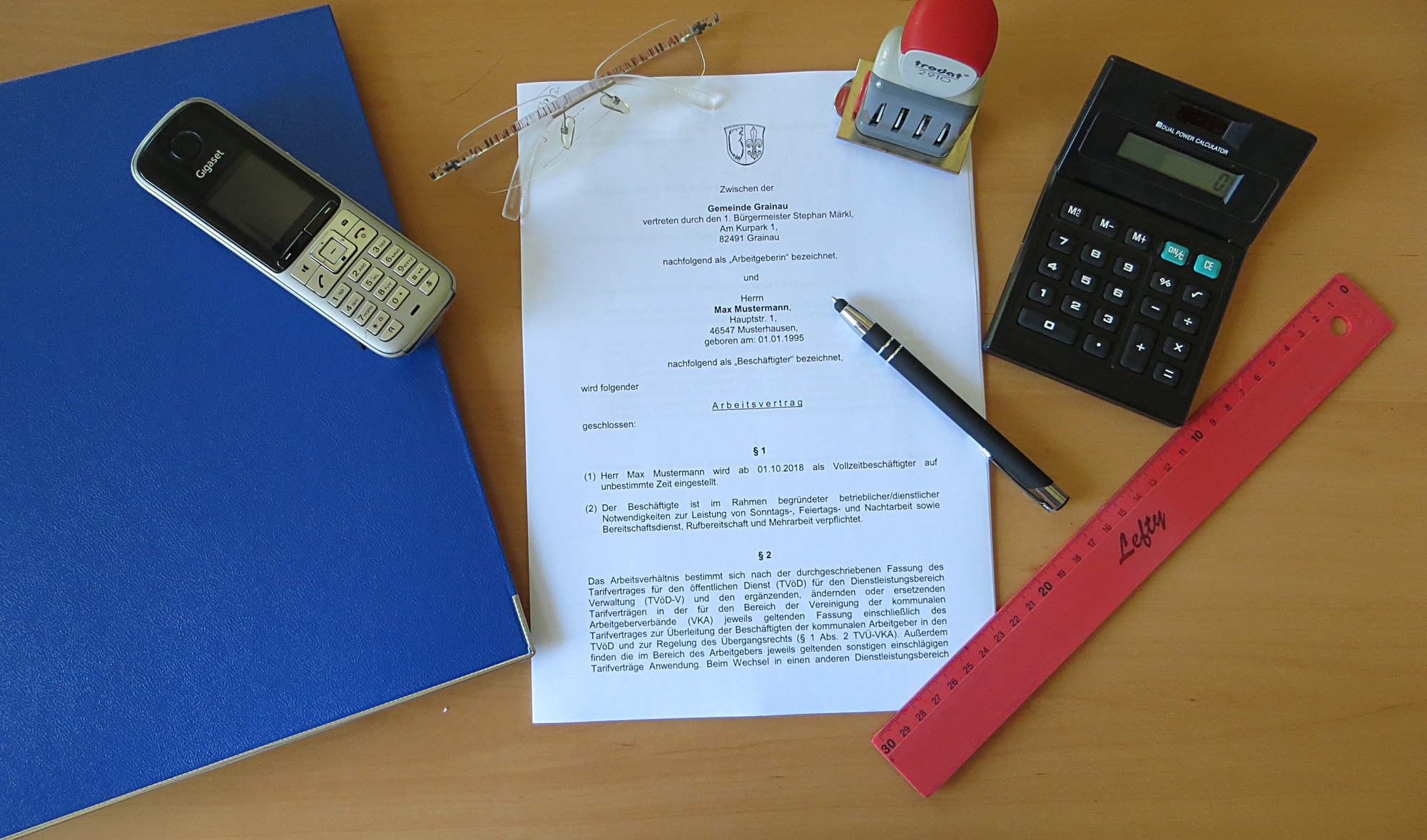 Grainau, Schreibtisch mit Arbeitsvertrag, Ordner, Telefon, Stift, Lineal, Stempel und Brille