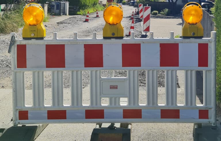 Grainau, Straßenabsperrung in weiß-rot, Gestell mit drei Warnlampen. Hintergrund aufgerissene Straße