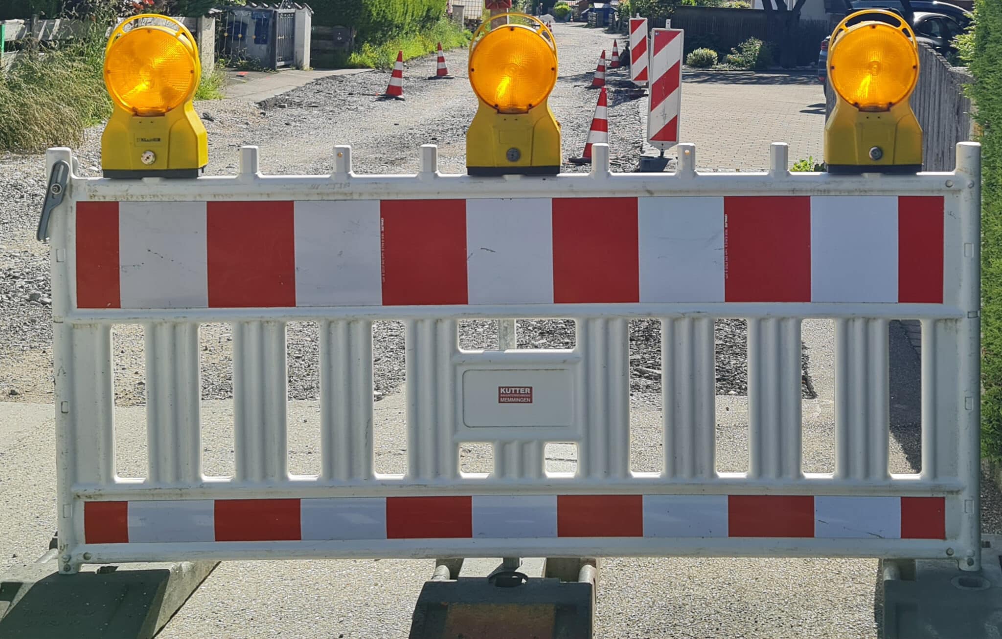 Grainau, Straßenabsperrung in weiß-rot, Gestell mit drei Warnlampen. Hintergrund aufgerissene Straße